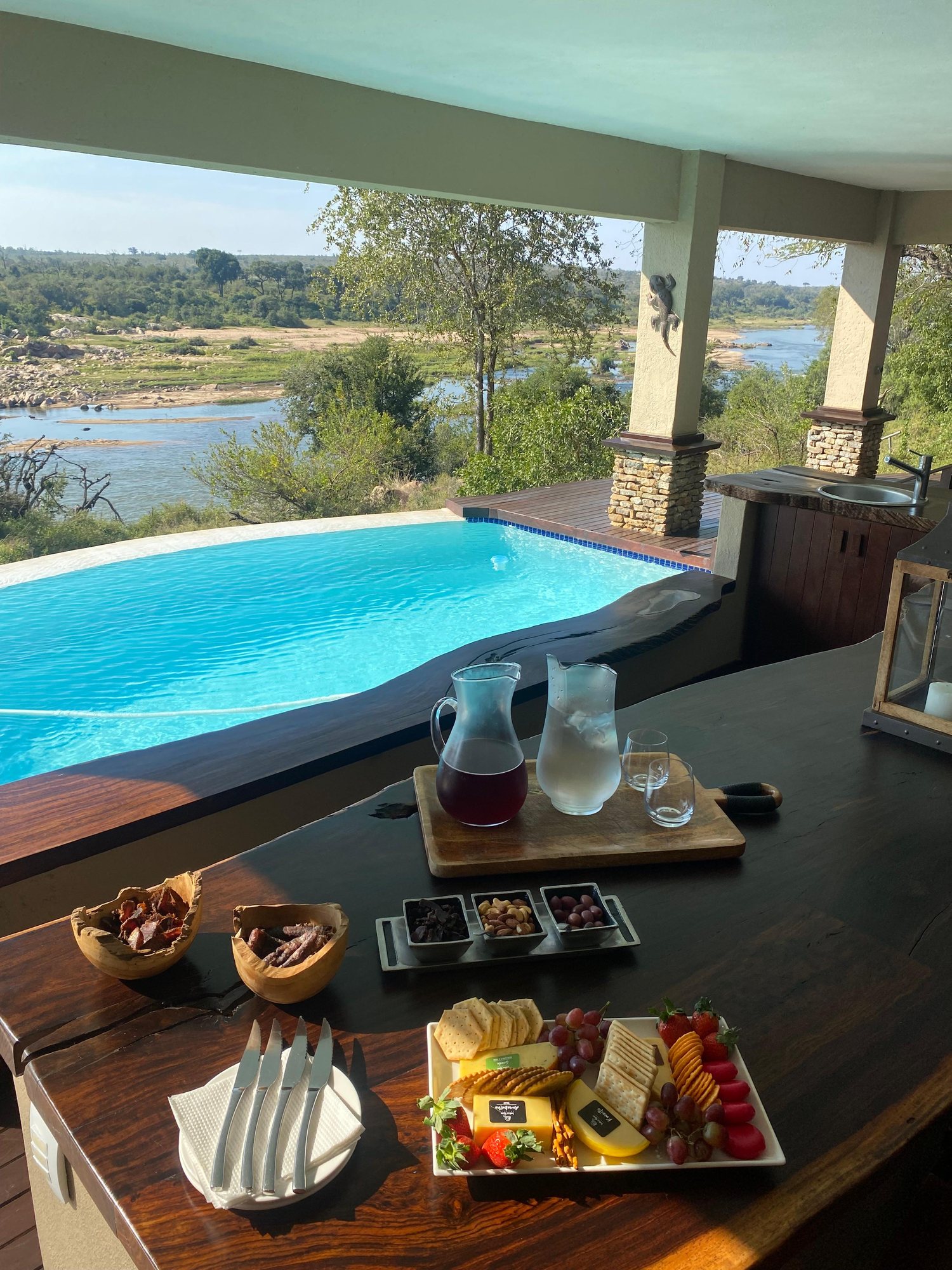Sundowners on the deck — a cheeseboard, drinks, the pool and river beyond